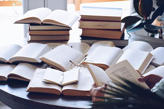 Photo of many books laying open on a circular table with a pair of glasses in the middle. 