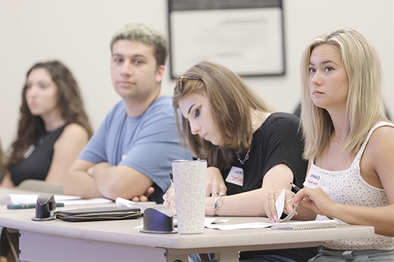 Several students seated together in a classroom, paying attention to an off-screen presentation