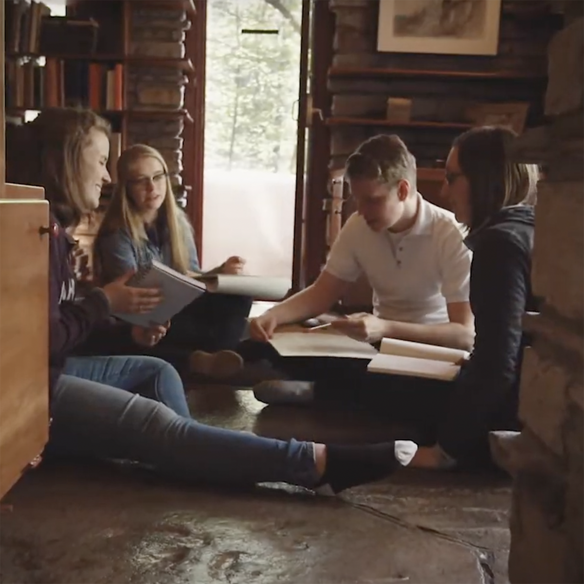 Photo of a group of students seated on the floor in Fallingwater, sketching and talking together