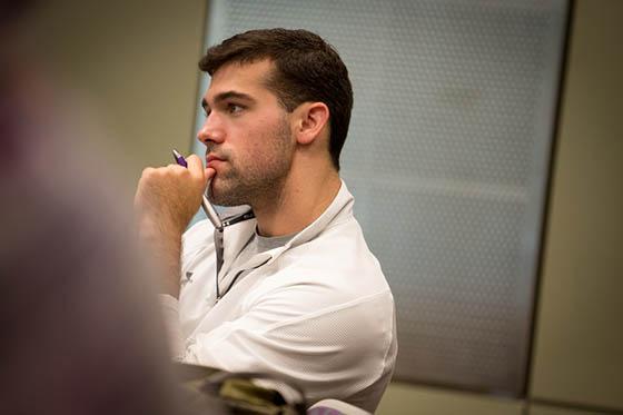 Photo of student in a white polo shirt, sitting with his hand to his chin paying attention to a lecture