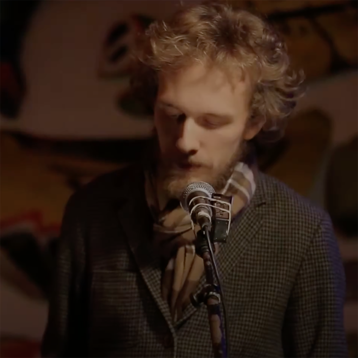 Photo of a man closing his eyes and looking down mid-poetry performance, with a microphone in front of him